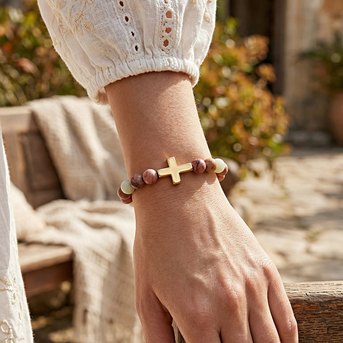 Hand wearing a bracelet with a cross charm in an outdoor setting
